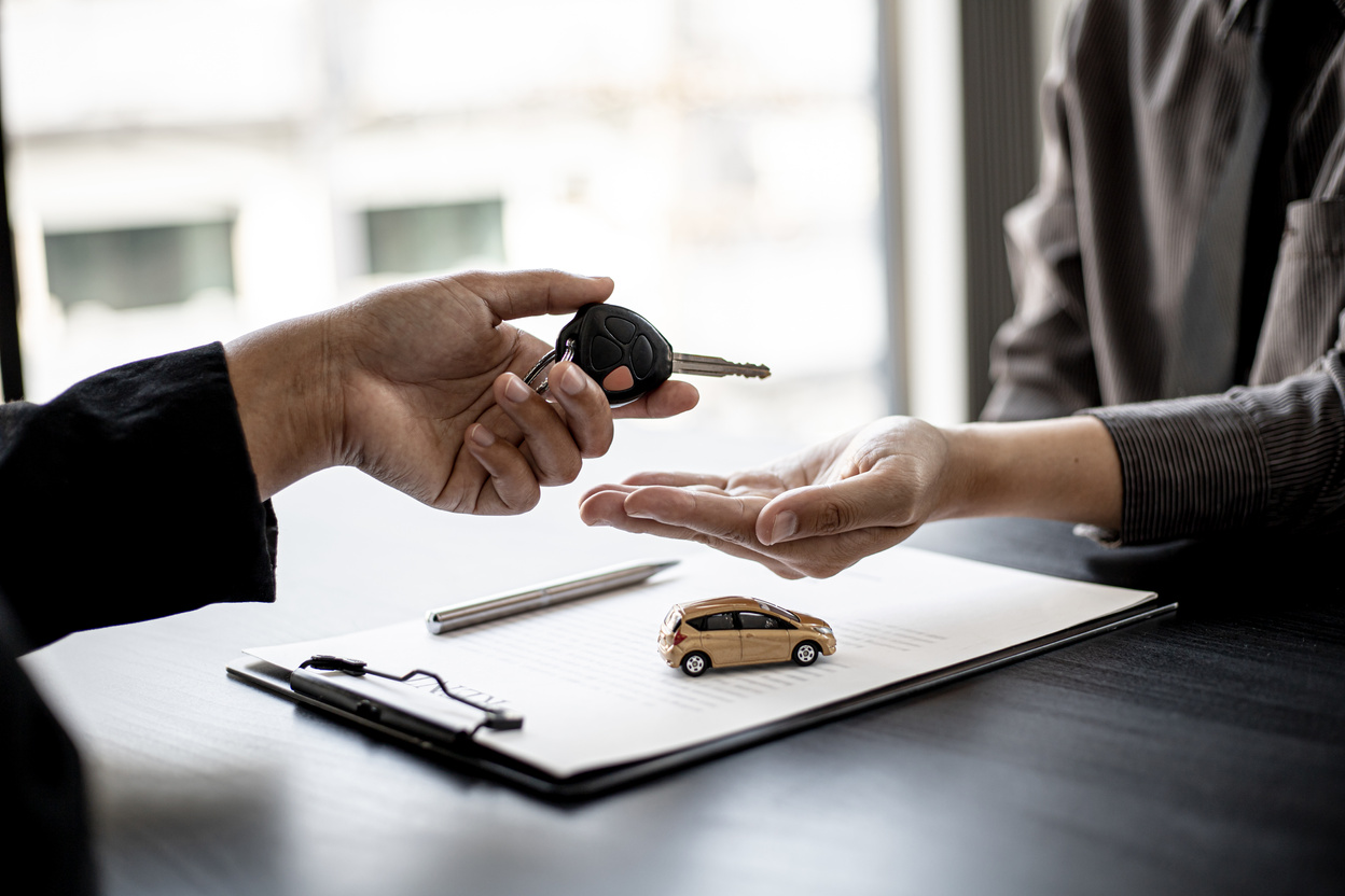 A car rental company employee is handing out the car keys to the renter after discussing the rental details and conditions together with the renter signing a car rental agreement. Concept car rental.